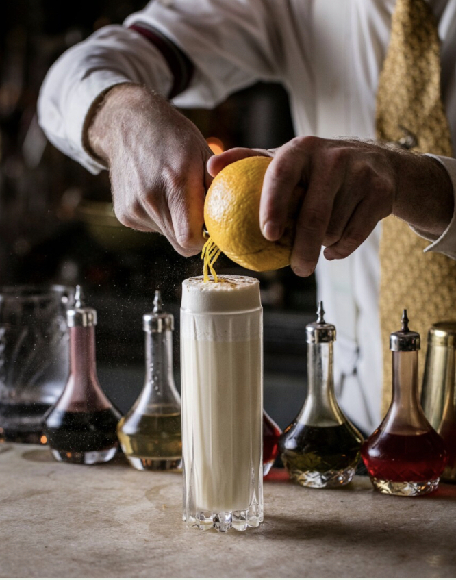 A mixologist slicing lemon skin into a cocktail