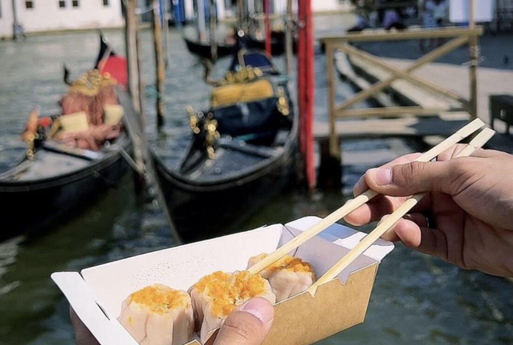 Man eating dumpling in Venice by water side, next to a boat in Venice